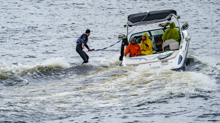 Russia, St. Petersburg, 29 July 2022: Man riding wakeboard on wave of motorboat in summer river, wakesurfing on river summertime leisureのeditorial素材