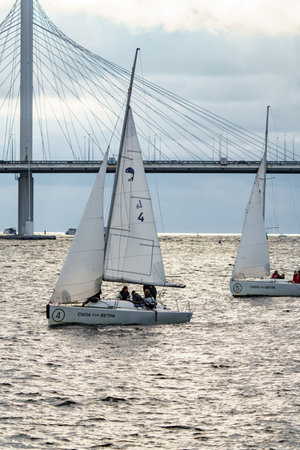 Russia, St. Petersburg, 29 July 2022: Few small sport sailing boats at sunset with stormy sky, sailing regatta, teamwork, hot pursuit, highly cable-stayed bridge on backgroundのeditorial素材