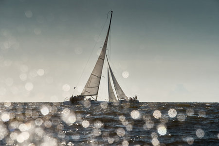 The view through the spray of how the two sailboats are heeling at sunset, boat roll, splashes shine in the sun, sailors on the boardsの写真素材