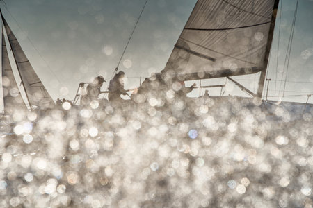 The view through the spray of how the two sailboats are heeling at sunset, boat roll, splashes shine in the sun, sailors on the boardsの写真素材
