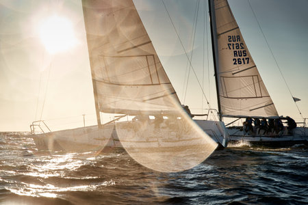 Russia, St.Petersburg 07 July 2023: The view through the spray of how few sailboats are heeling at sunset, boat roll, splashes shine in the sun, sailors on the boardsのeditorial素材