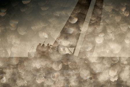 The view through the spray of how the sailboat is heeling at sunset, boat roll, splashes shine in the sun, sailors on the boardの写真素材