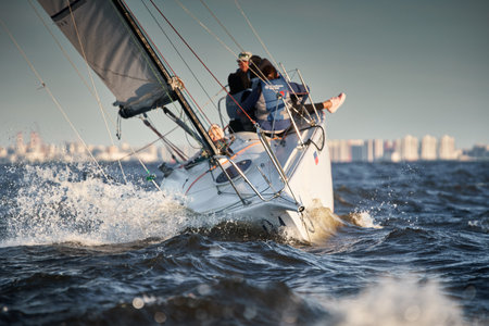 Russia, St.Petersburg, 07 July 2023: The view through the spray of how the sailboat is heeling at sunset, boat roll, splashes shine in the sun, sailors on the boardのeditorial素材