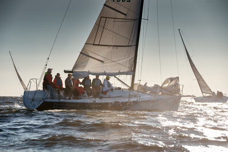 Russia, St.Petersburg 07 July 2023: The view through the spray of how few sailboats are heeling at sunset, boat roll, splashes shine in the sun, sailors on the boardsのeditorial素材