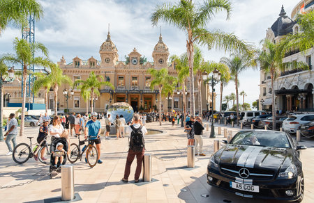 Monaco, Monte-Carlo, 29 September 2022 - Square Casino Monte-Carlo at sunny day, luxury cars, famous Hotel de Paris, wealth life, tourists take pictures of the landmark, pine trees, flowersのeditorial素材