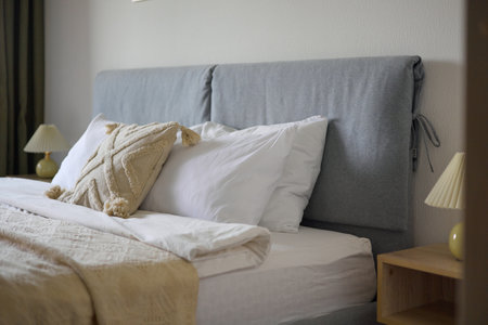 Cozy bedroom interior, beige bedspread and pillow, bedside lamp next to the bed, light from the windowの写真素材