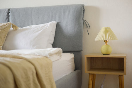 Cozy bedroom interior, beige bedspread and pillow, bedside lamp next to the bed, light from the...