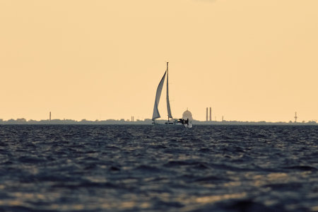 The lonely sailboat at sunset, the Naval Cathedral in Kronstadt on background, Sailing regatta in the Gulf of Finland at sunset, sailing yacht competing in a race, splashing water, board the boatの写真素材