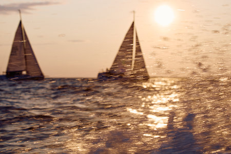 Sailing regatta in the Gulf of Finland at sunset, two sailing yachts competing in a race, splashing water from under the boats, teamwork, board the boatの写真素材
