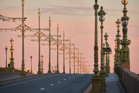 rows of lampposts and poles with electric grids for a tram on an empty Troitskiy Bridge at a pink sunset, nobodyの写真素材