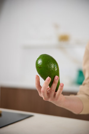 A large avocado in a womans hand in the interiors of a bright and spacious kitchenの写真素材