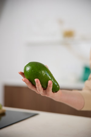 A large avocado in a woman's hand in the interiors of a bright and spacious kitchenの写真素材