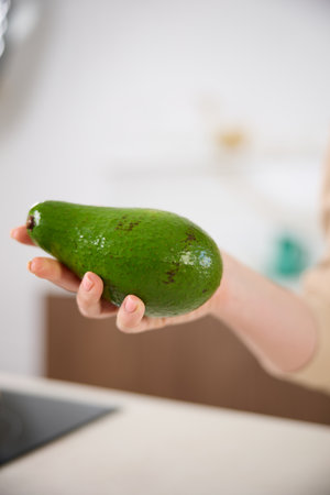 A large avocado in a womans hand in the interiors of a bright and spacious kitchenの写真素材