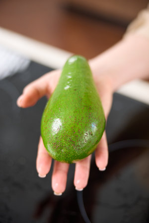 A large avocado in a woman's hand in the interiors of a bright and spacious kitchenの写真素材