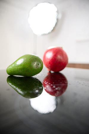 A fresh green avocado and a red garnet lies on a glass table