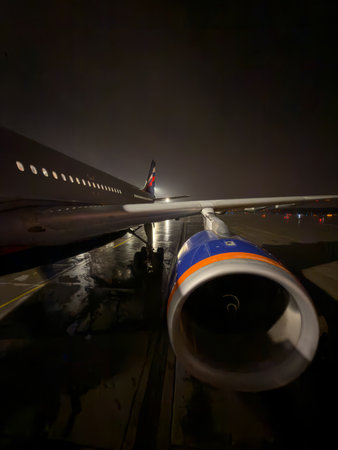 the plane is standing on the airport runway at night, many passengers are walking down the ramp to board the plane, a huge turbine on the wing of the aircraftの写真素材