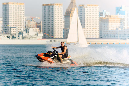 Russia, St.Petersburg, 26 July 2024: athletic men rides a jet ski with splashes, he is having fun on...