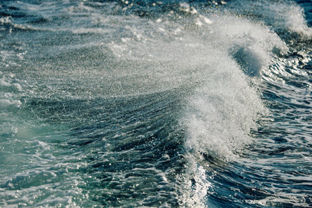 A wave breaks against a strong wind in sunny weather
