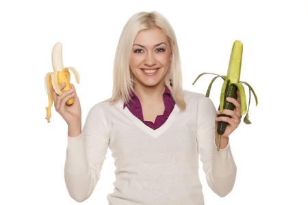 beautiful girl hesitating about bananas and cucumbers on white backgroundの写真素材