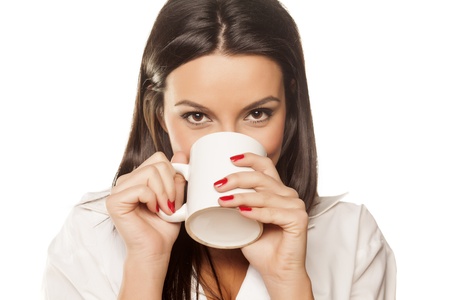 smiling beautiful brunette in a white men s shirt drinking coffee and showing his thumbの写真素材