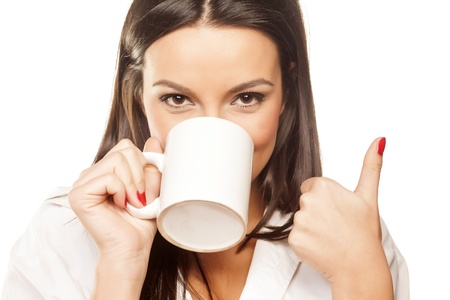 surprised beautiful brunette in a white shirt drinks tea and shows thumbの写真素材