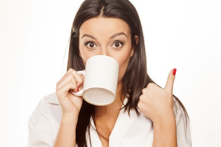 surprised beautiful brunette in a white shirt drinks tea and shows thumbの写真素材