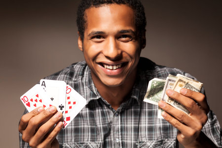 african young man holds the winning combination of poker cards in one hand and wade of money in the...