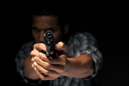 dark-skinned young man aiming with his gun at youの写真素材