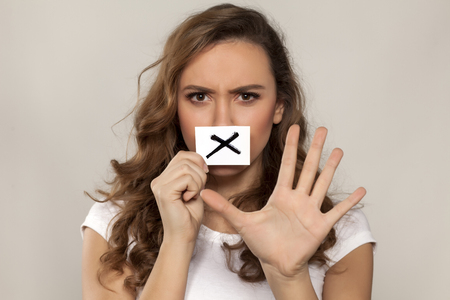 nervous young girl with X sign drawn on a paper over her mouthの写真素材