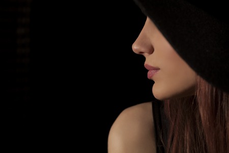 profile of woman with a hat posing on a dark backgroundの写真素材