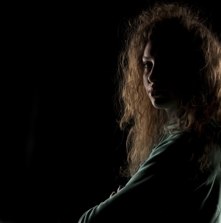 portrait of a girl with the face in shadow on a dark backgroundの写真素材