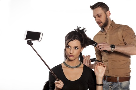 girl making selfie while hairdresser blow-dry her hairの写真素材