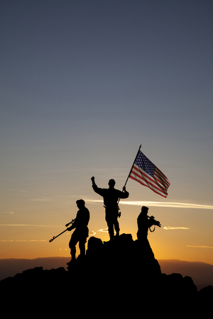 Three armed soldiers with the American flag on the top of the mountainの写真素材