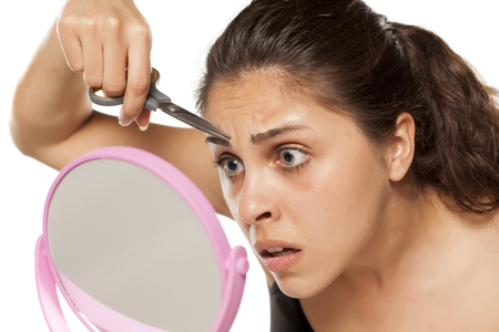 young woman shaping her eyebrows using scissorsの写真素材