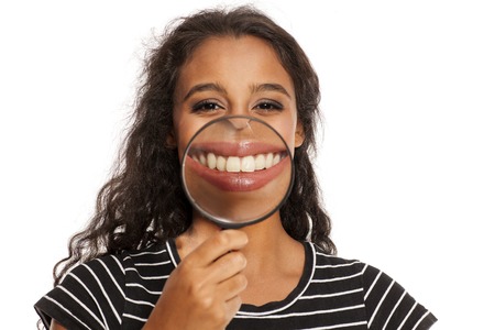 Beautiful young dark skinned woman holding a magnifying glass front of her mouthの写真素材