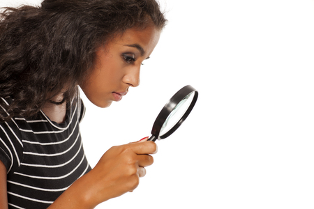 Beautiful young dark skinned woman looking trough the magnifying glassの写真素材