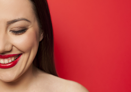 half portrait of beautiful smiling woman with makeup on red backgroundの写真素材