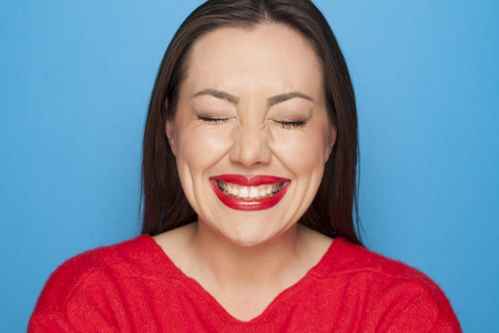 beautiful ashamed woman in a red blouse on a blue backgroundの写真素材