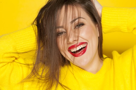 beautiful happy woman in a yellow sweater on a yellow backgroundの写真素材
