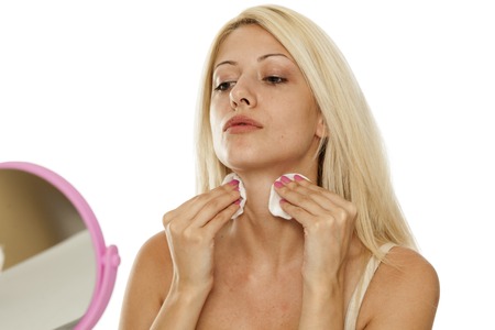 young woman cleaning her neck with cotton pad osn white backgroundの写真素材