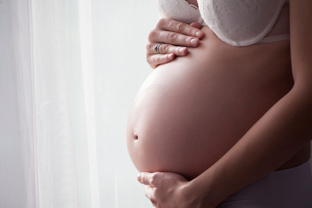 belly of a pregnant woman beside the window with curtains