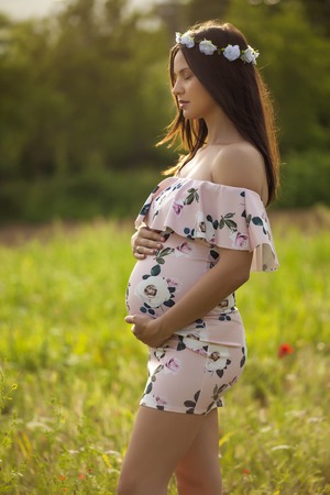 Pregnant calm woman on a meadow with wreaths of flowers on her headの写真素材