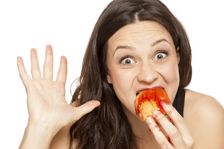 A giddy young woman eats a donut with an topping of cherry on a white backgroundの写真素材