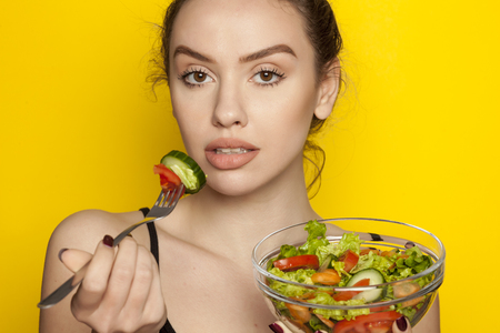 Young beautiful woman eating salad on white backgroundの写真素材