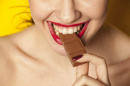 Young beautiful woman eating a chocolate on yellow backgroundの写真素材