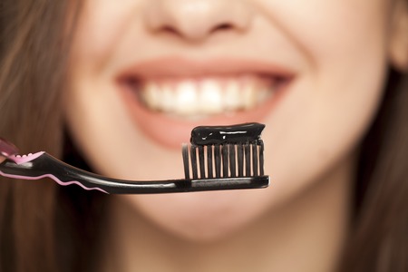 young woman holding a black tooth paste with active charcoal, and black tooth brush on white backgroundの写真素材