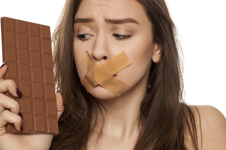 young woman longs looking at chocolate with taped mouth on white backgroundの写真素材