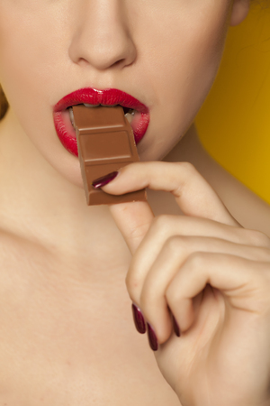 Young beautiful woman eating a chocolate on yellow backgroundの写真素材