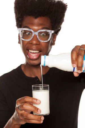 Portrait of young african american man pouring a glass with yogurt on white background