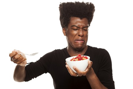 disgusted young handsome afro american guy hipster eating cereals woth fresh fruits isolated on white background. healthy food conceptの写真素材